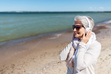 Image showing old woman in headphones listens to music on beach