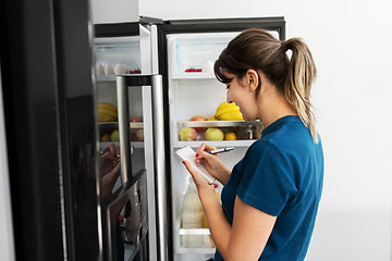 Image showing woman making list of necessary food at home fridge