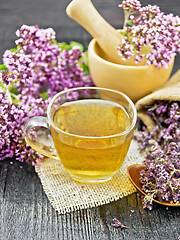 Image showing Tea of oregano in cup with mortar on dark wooden board