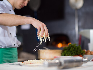 Image showing chef sprinkling cheese over fresh pizza dough