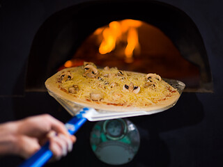 Image showing chef putting delicious pizza to brick wood oven