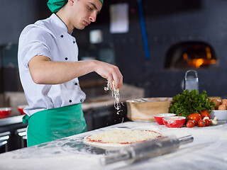 Image showing chef sprinkling cheese over fresh pizza dough