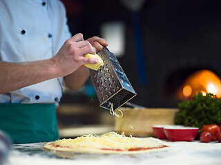 Image showing chef sprinkling cheese over fresh pizza dough