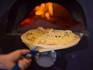 Image showing chef putting delicious pizza to brick wood oven