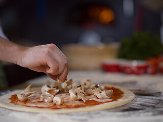 Image showing chef putting fresh mushrooms on pizza dough