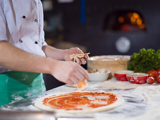 Image showing chef putting cut sausage or ham on pizza dough
