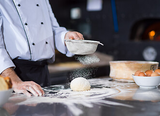 Image showing chef sprinkling flour over fresh pizza dough