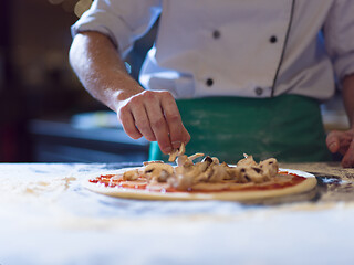 Image showing chef putting fresh mushrooms on pizza dough