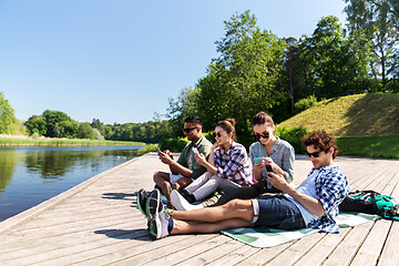 Image showing friends with smartphone on lake pier in summer