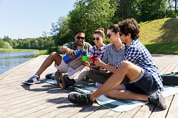 Image showing happy friends drinking tea from thermos in summer