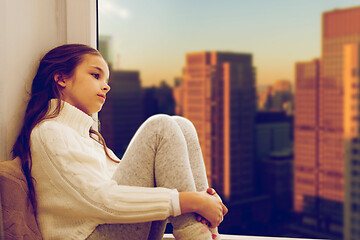 Image showing sad girl sitting on sill at home window over city