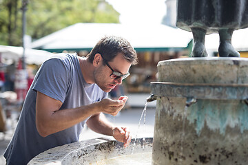 Image showing Thirsty young casual cucasian man drinking water from public city fountain on a hot summer day