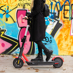 Image showing Trendy teenage girl riding public rental electric scooter in urban city environment at fall. New eco-friendly modern public city transport in Ljubljana