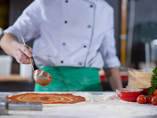 Image showing Chef smearing pizza dough with ketchup