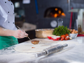 Image showing Chef smearing pizza dough with ketchup