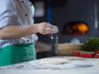 Image showing chef sprinkling flour over fresh pizza dough