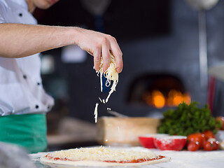 Image showing chef sprinkling cheese over fresh pizza dough