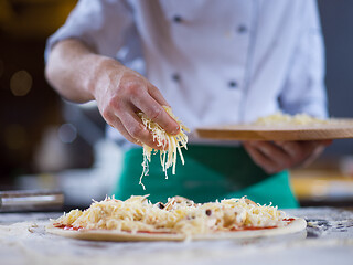 Image showing chef sprinkling cheese over fresh pizza dough