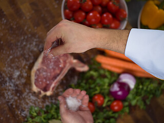 Image showing Chef putting salt on juicy slice of raw steak