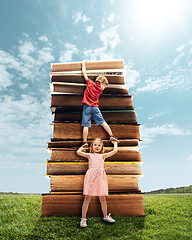 Image showing Little girl and boy climbing on the tower made of big books