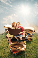 Image showing Little girl and boy sitting on the tower made of big books