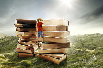 Image showing Little boy climbing on the tower made of big books