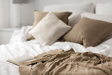 Image showing bed with pillows, blanket and open book at home