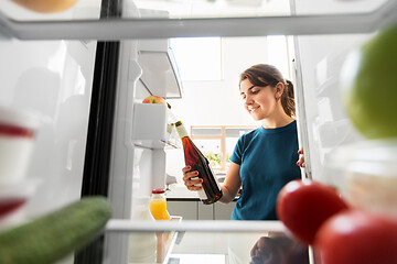 Image showing happy woman taking wine bottle from fridge at home