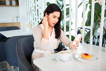 Image showing asian woman with smartphone and earphones at cafe