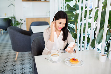 Image showing asian woman with smartphone and earphones at cafe