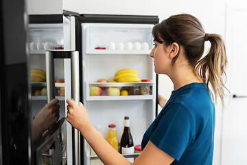 Image showing woman at open fridge at home kitchen