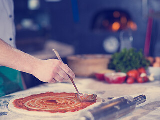 Image showing Chef smearing pizza dough with ketchup