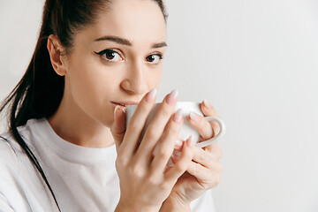 Image showing Taking a coffee break. Handsome young man holding coffee cup while standing against gray background