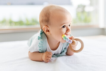 Image showing baby girl on white blanket chewing wooden rattle