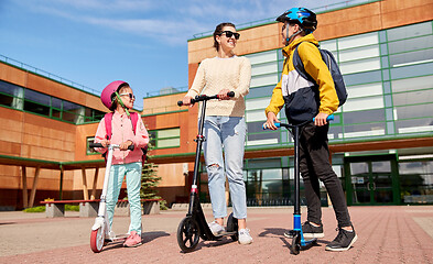 Image showing happy school children with mother riding scooters