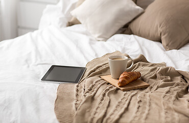 Image showing tablet pc, coffee cup and croissant on bed at home