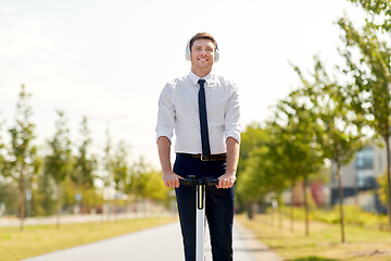 Image showing businessman with headphones riding scooter in city