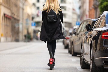 Image showing Rear view of girl riding public rental electric scooter in urban city environment. New eco-friendly modern public city transport in Ljubljana