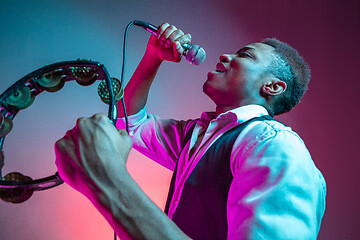 Image showing African American handsome jazz musician playing tambourine and singing.