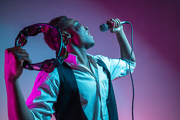 Image showing African American handsome jazz musician playing tambourine and singing.