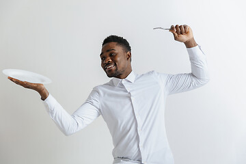 Image showing Young smiling attractive african american guy holding empty dish and fork isolated on grey background. Copy space and mock up. Blank template background.