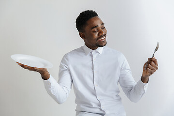 Image showing Young smiling attractive african american guy holding empty dish and fork isolated on grey background. Copy space and mock up. Blank template background.