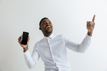 Image showing Indoor portrait of attractive young black african man isolated on pink background, holding blank smartphone, smiling at camera, showing screen, feeling happy and surprised. Human emotions, facial