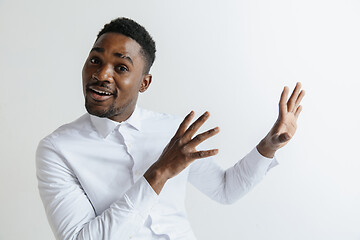 Image showing Handsome Afro American man in classic shirt is smiling, looking at camera and pointing away, against white brick wall