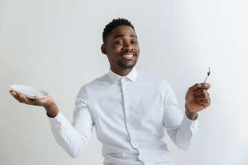 Image showing Young smiling attractive african american guy holding empty dish and spoon isolated on grey background. Copy space and mock up. Blank template background.