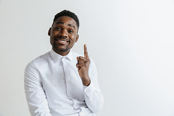 Image showing Handsome Afro American man in classic shirt is smiling, looking at camera and pointing away, against white brick wall