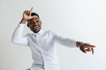 Image showing Losers go home. Portrait of happy guy showing loser sign over forehead and smiling in cause of victory and laughing over gray background