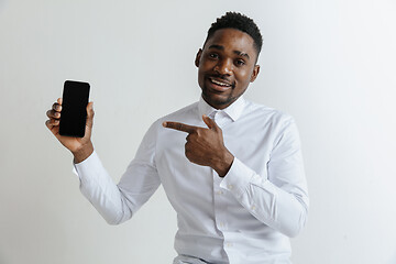 Image showing Indoor portrait of attractive young black african man isolated on pink background, holding blank smartphone, smiling at camera, showing screen, feeling happy and surprised. Human emotions, facial