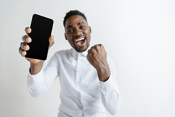 Image showing Indoor portrait of attractive young black african man isolated on pink background, holding blank smartphone, smiling at camera, showing screen, feeling happy and surprised. Human emotions, facial