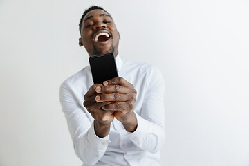 Image showing Indoor portrait of attractive young black african man isolated on pink background, holding blank smartphone, smiling at camera, showing screen, feeling happy and surprised. Human emotions, facial